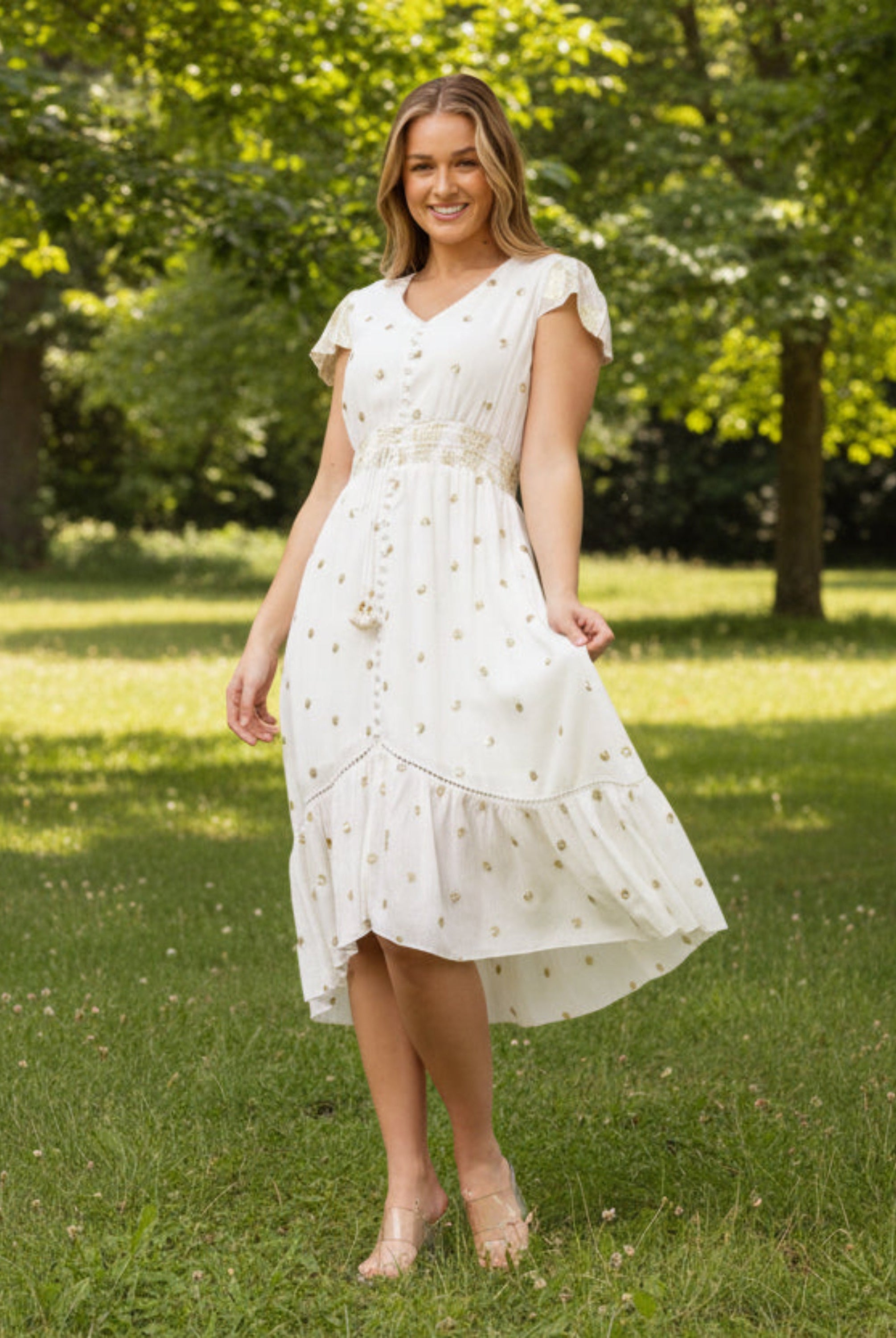 Woman in a white dress standing in a park with green grass and trees.