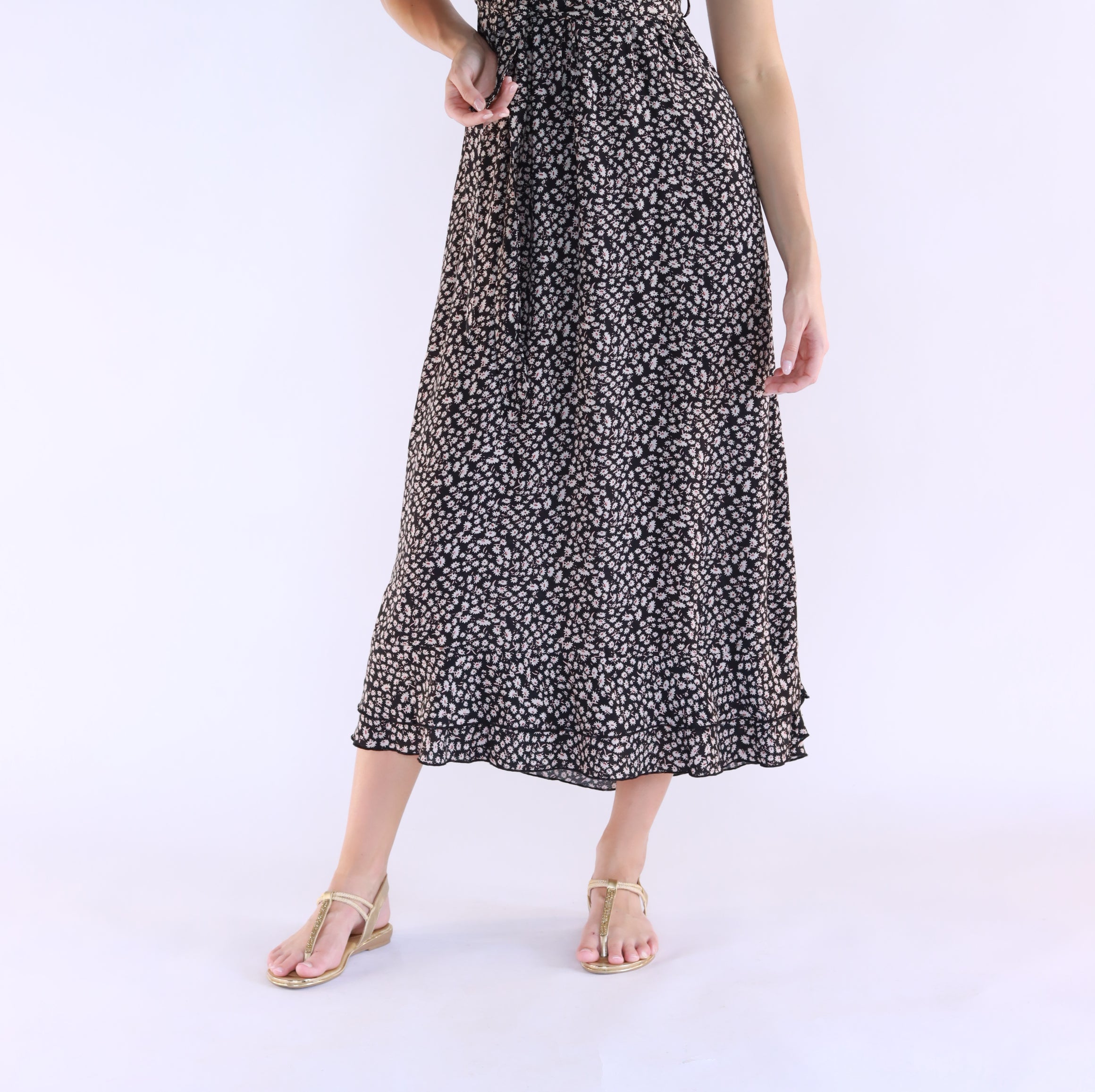 A woman standing wearing a floral maxi dress with a V-neckline and sleeveless design.