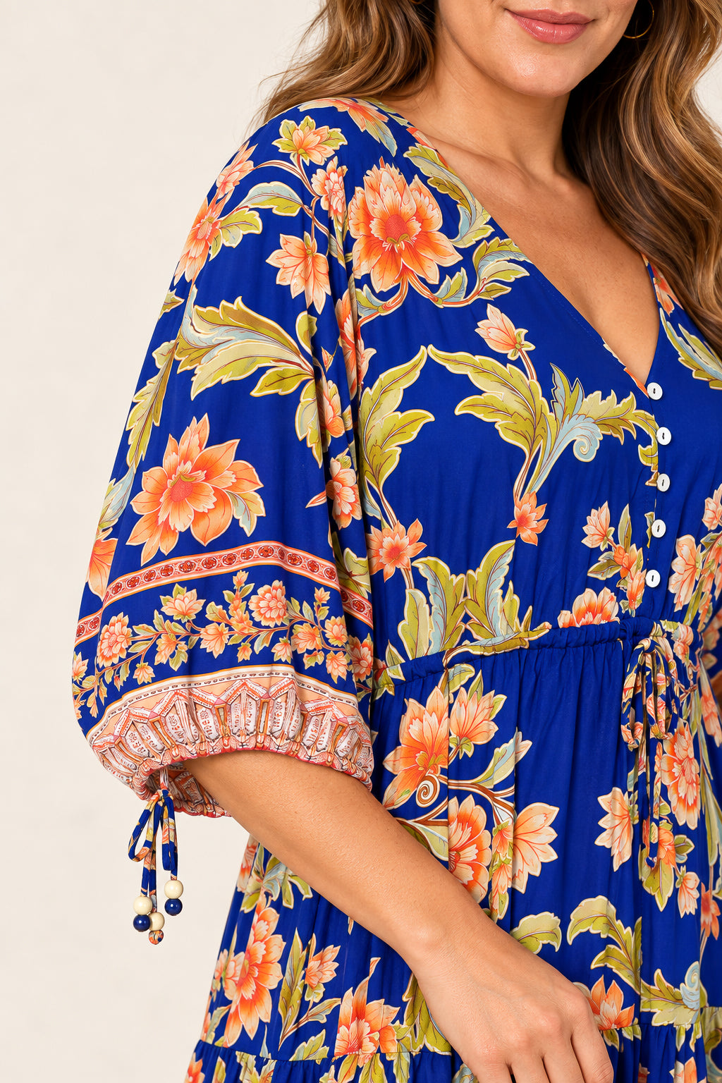 A close-up of a woman wearing a vibrant royal blue dress with a bold orange and yellow floral print, featuring puff sleeves with tie details and a buttoned V-neckline.