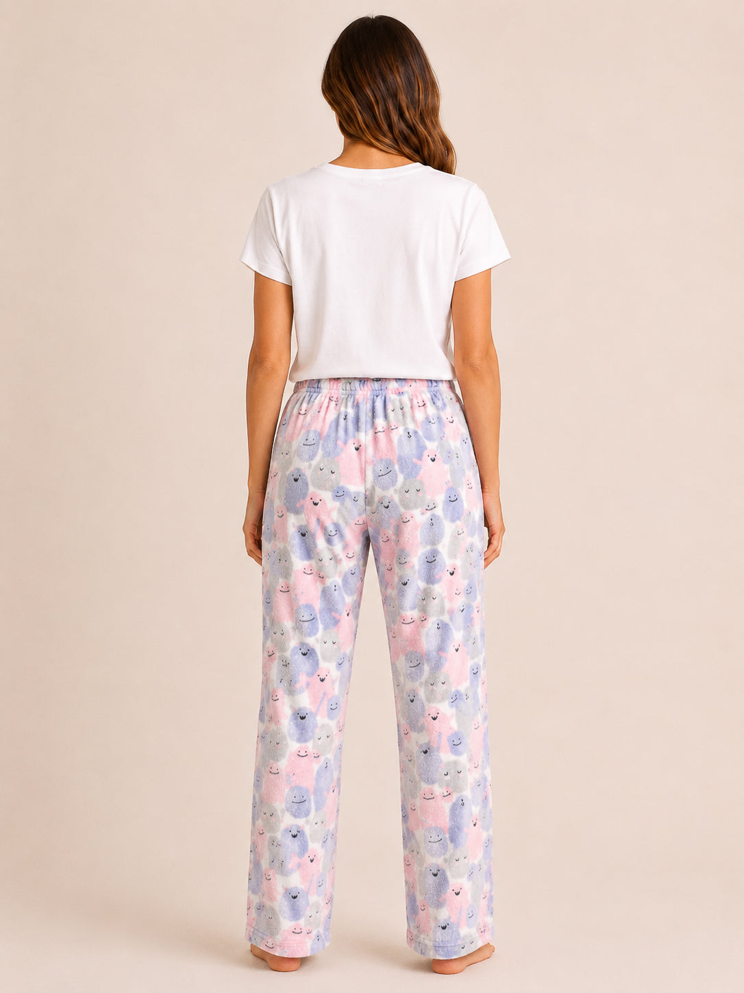 A woman viewed from behind wearing a white short-sleeve T-shirt and loose, wide-leg pajama pants with a pastel elephant print on a light background.