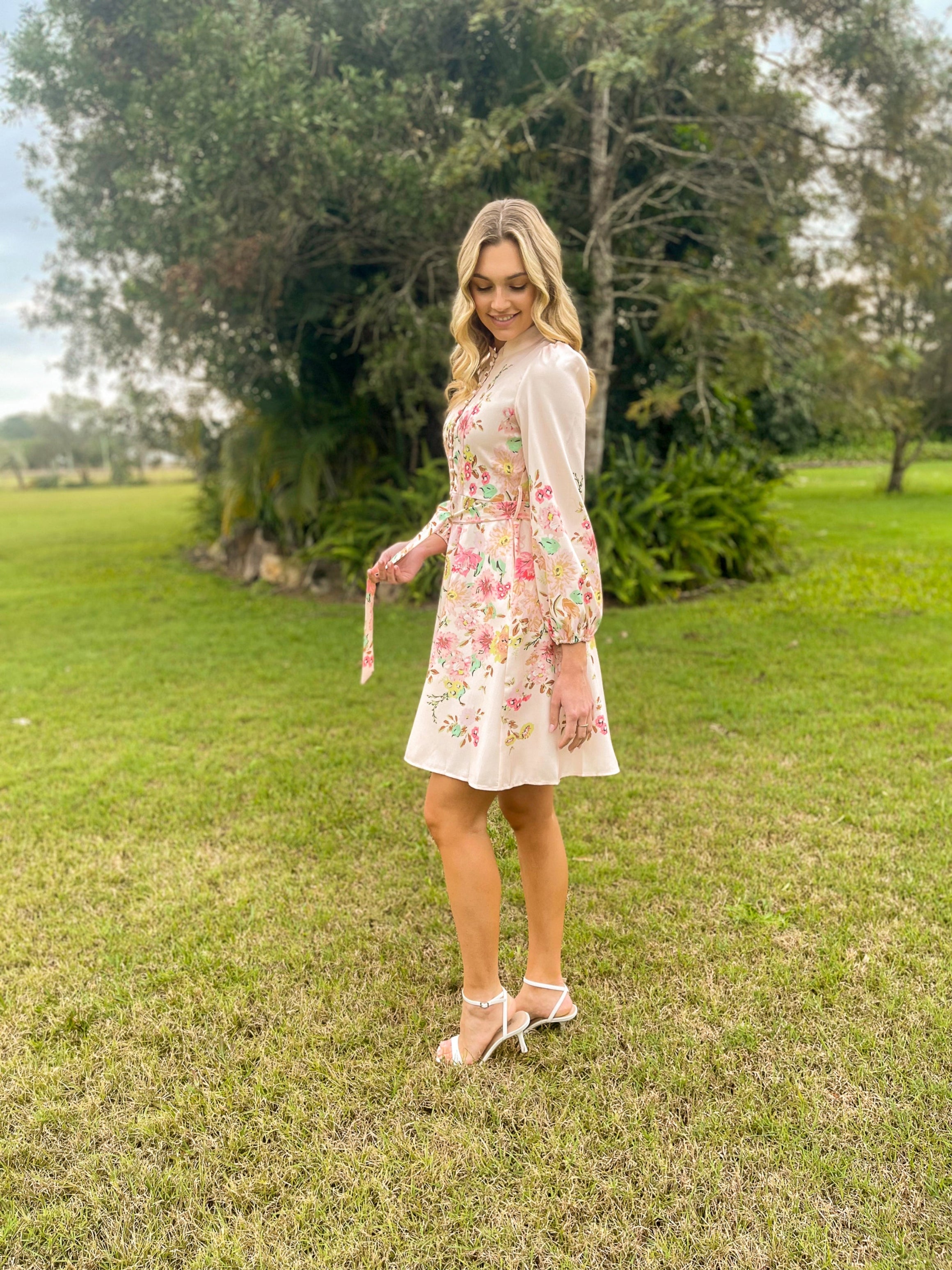 Woman in a floral dress standing in a grassy area with trees in the background