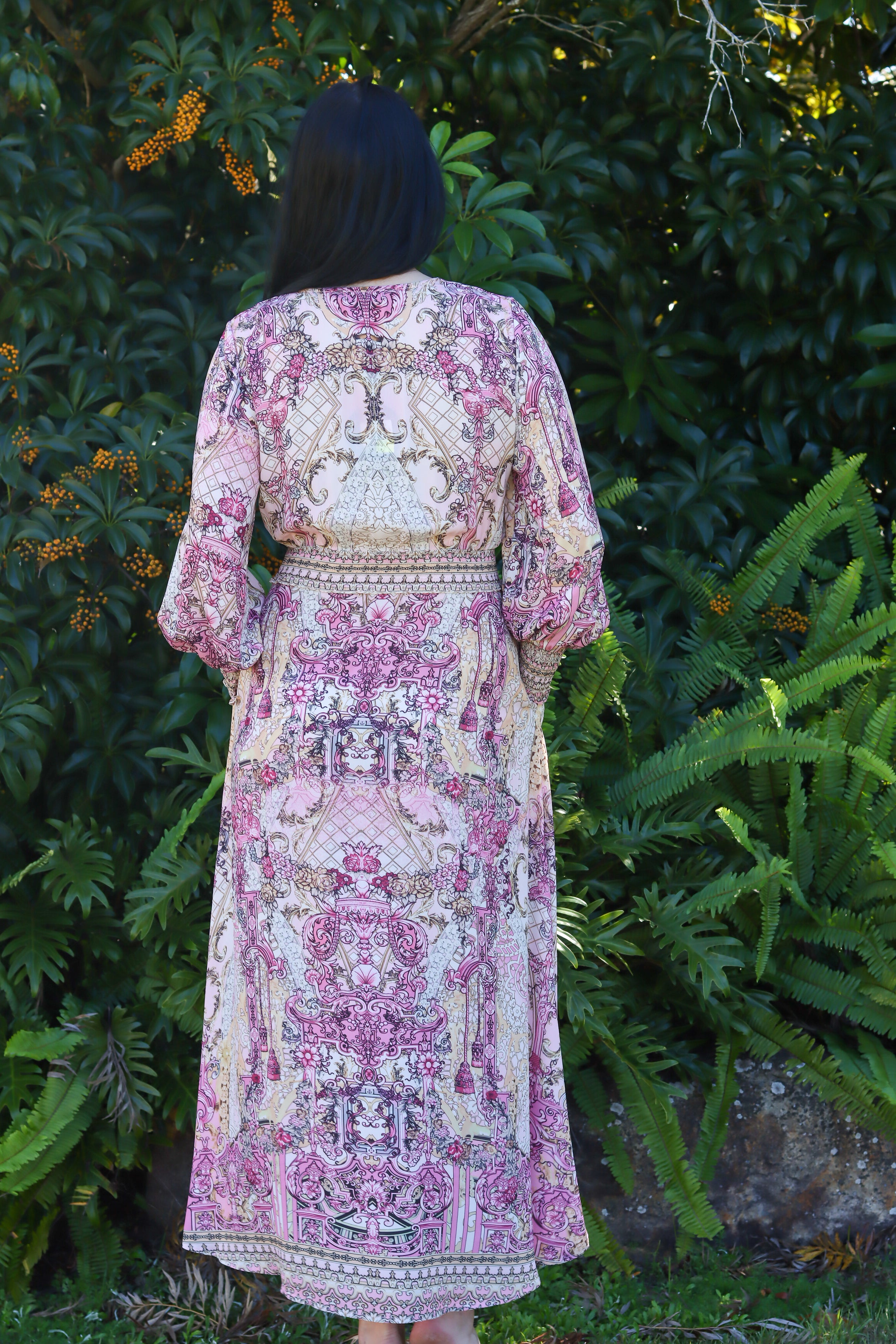 Person wearing a patterned dress standing in a garden with greenery.