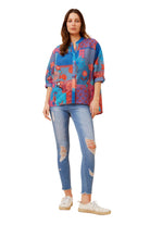 Woman wearing a colorful patterned shirt and blue jeans on a white background