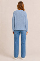 Person wearing a blue knitted sweater and jeans on a beige background