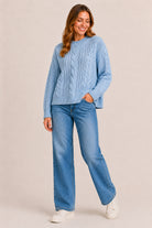 Woman wearing a blue cable knit sweater and jeans on a beige background