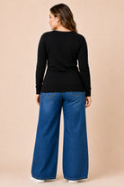 Woman wearing a black long-sleeve top and blue jeans on a beige background