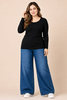 Woman wearing a black long-sleeve top and blue jeans on a beige background