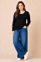 Woman wearing a black sweater and blue jeans against a beige background