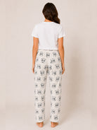 A woman viewed from behind wearing a white t-shirt and white pants with a gray panda print, standing against a plain beige studio background.