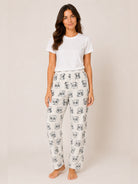A woman modeling a pair of white lounge pants with a black and gray panda print, paired with a plain white t-shirt, against a solid light beige background.