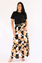 Woman wearing a black top and a long, patterned skirt on a white background