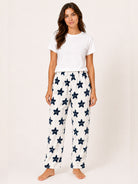 A woman modeling a two-piece pajama set consisting of a white short-sleeve t-shirt and white lounge pants with a navy blue star pattern, shot against a solid off-white studio background.